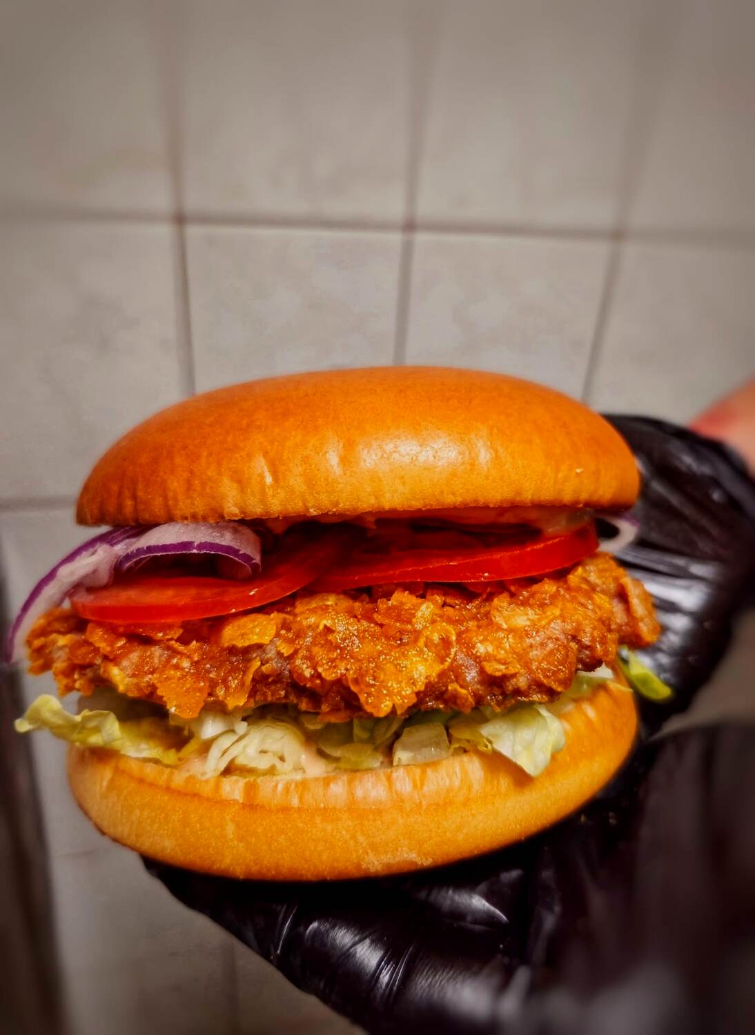 Ropogós csirkés burger kézben, friss zöldségekkel