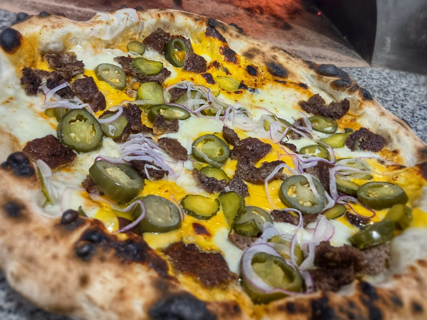 Egész La Smashera pizza a kemence szája előtt, jalapenóval, csemegeuborkával és smashed marhahússal