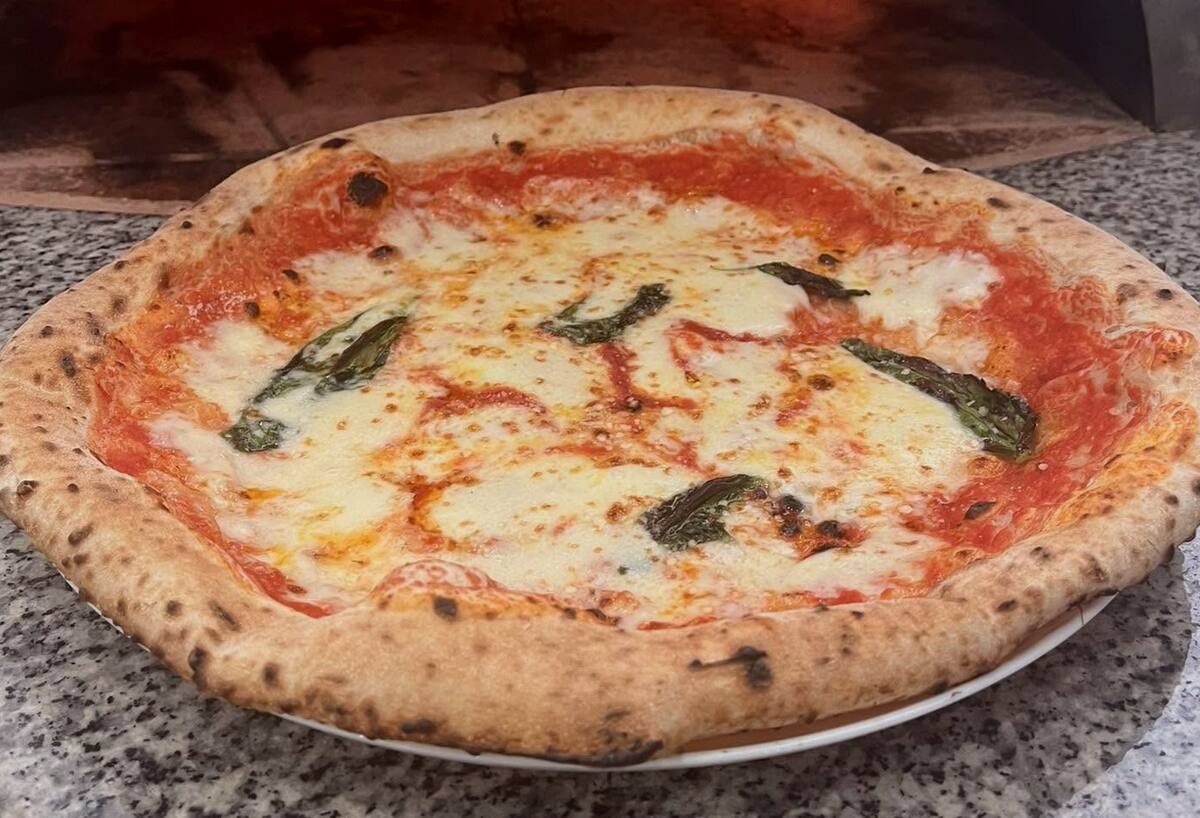 Egész margherita pizza tányéron, a kemence előtt