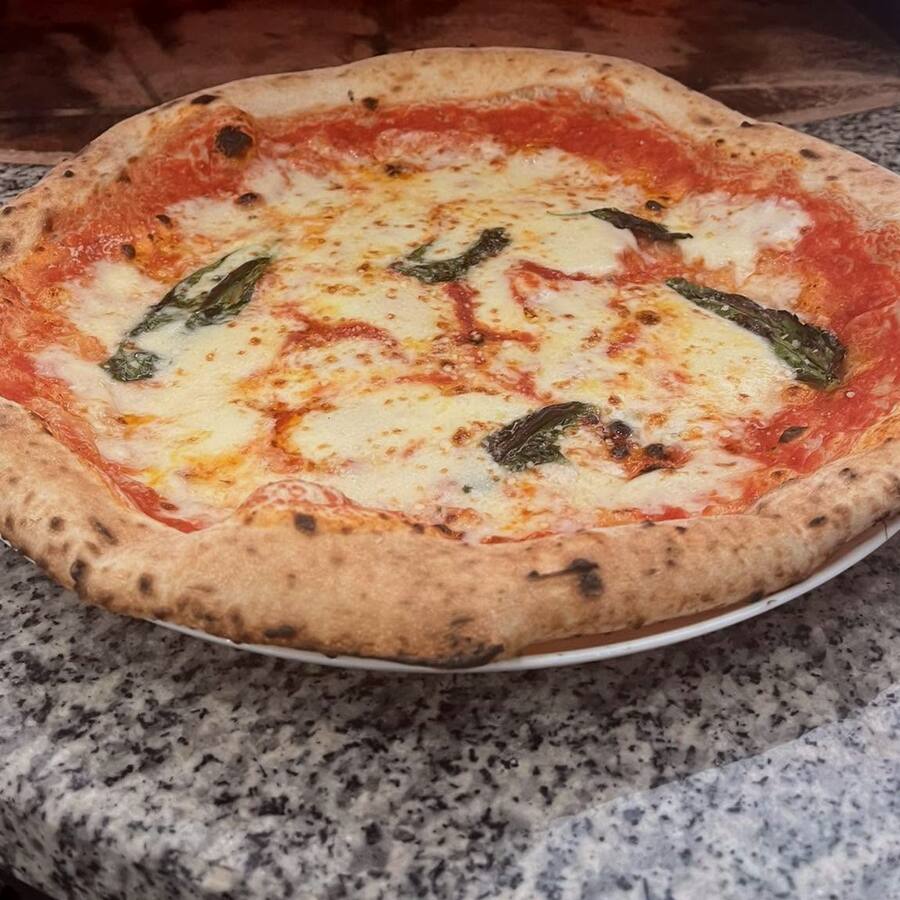 Egész margherita pizza tányéron, a kemence előtt